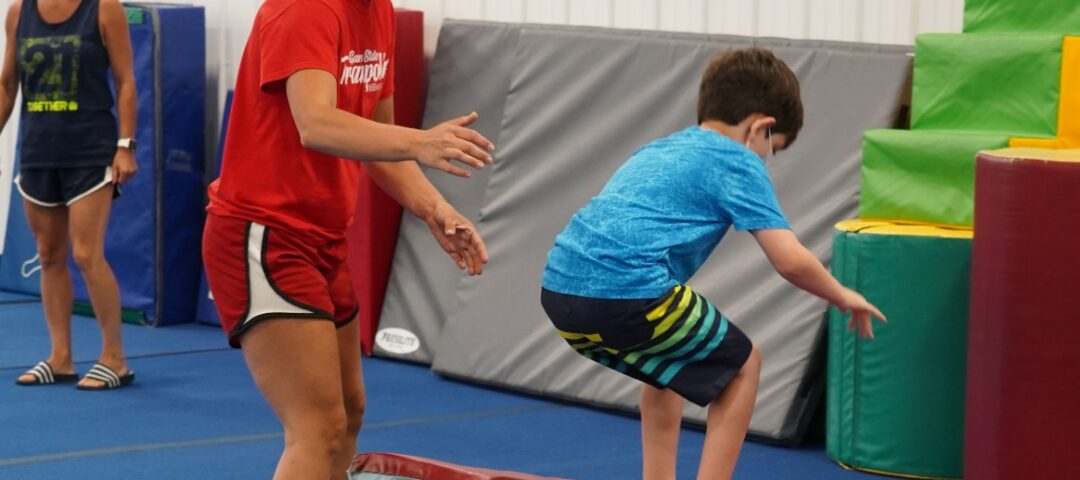 Coach Nastia in a mask helps a child do a backflip.