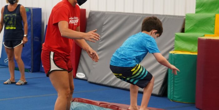 Coach Nastia in a mask helps a child do a backflip.