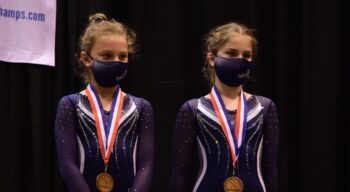 Two girls stand at a podium with medals.