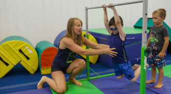 nastia helping a boy swing on bars.