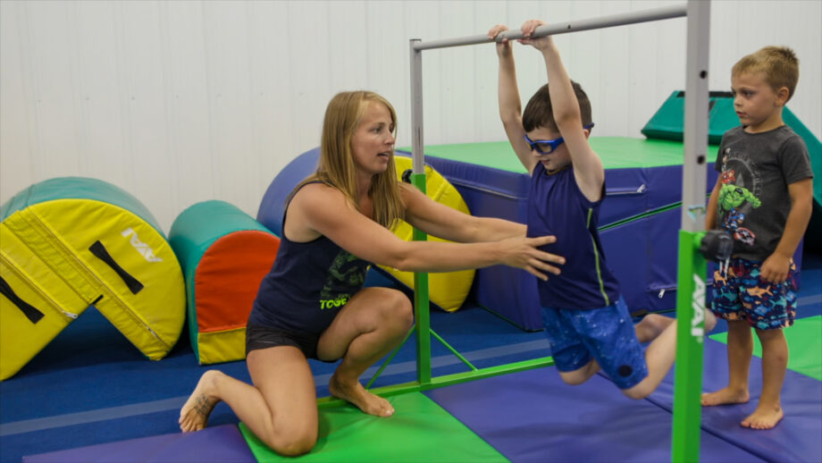 nastia helping a boy swing on bars.