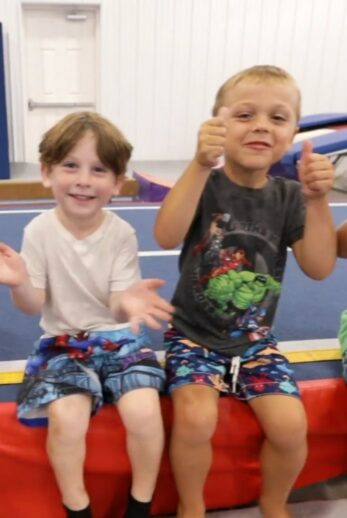 Two boys sitting and waving at the camera.