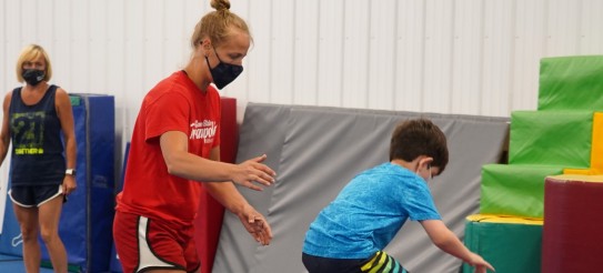 Coach Nastia in a mask helps a child do a backflip.